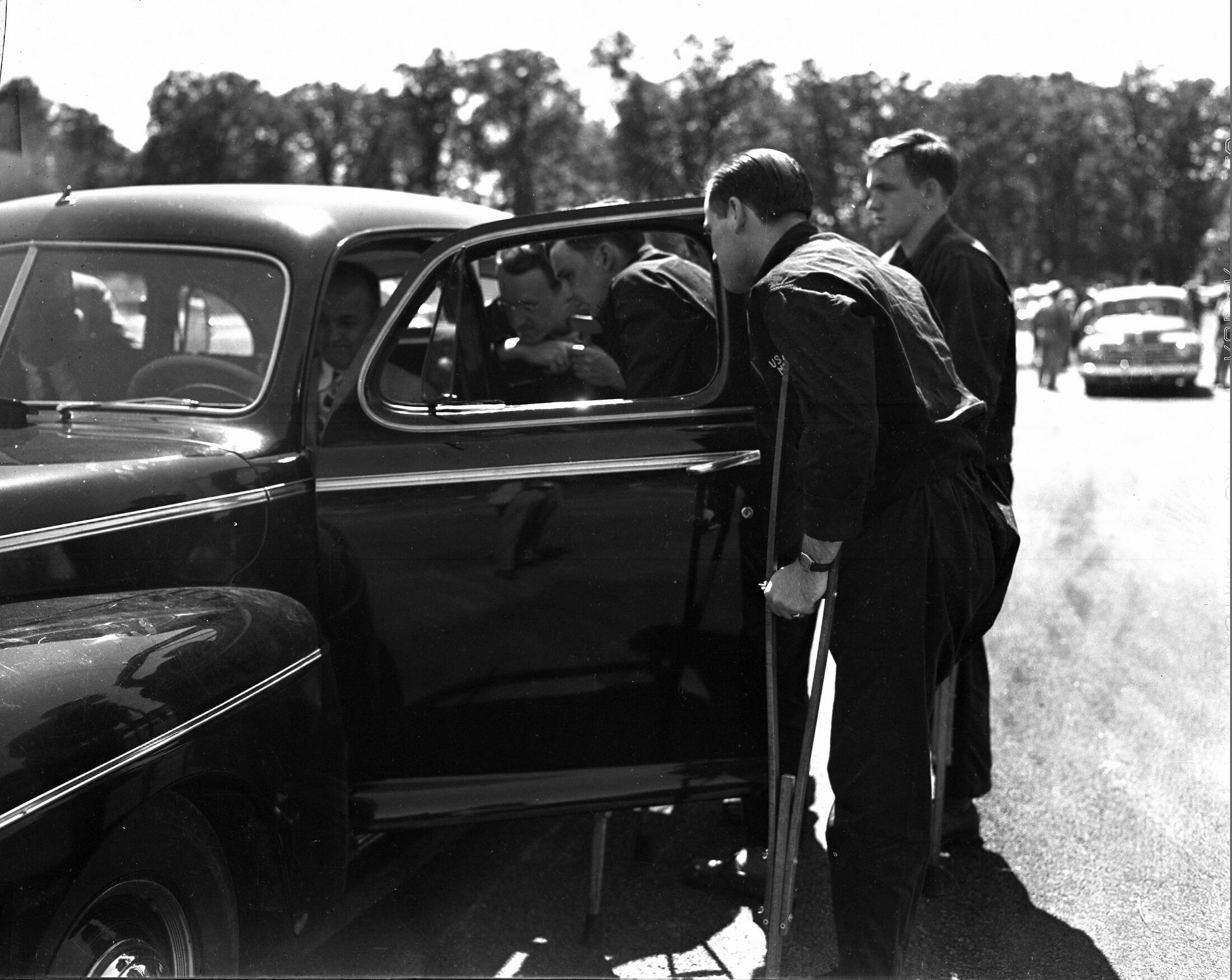 Man with crutches looking inside 1945 Ford vehicle